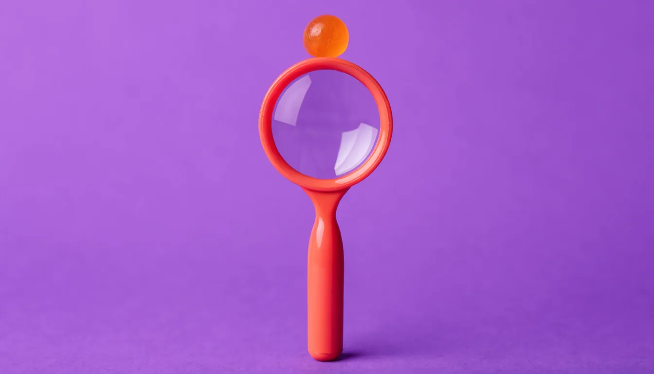 A single bright candy-coloured magnifying glass with a cheerful plastic handle centred on a solid purple background.