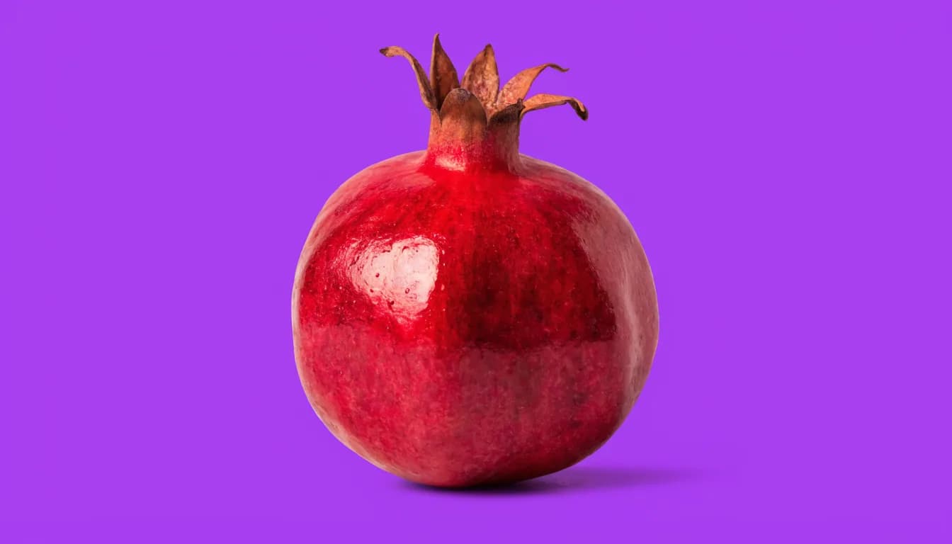 A single whole glossy pomegranate centred on a solid purple background, soft studio light with a gentle drop shadow beneath it.
